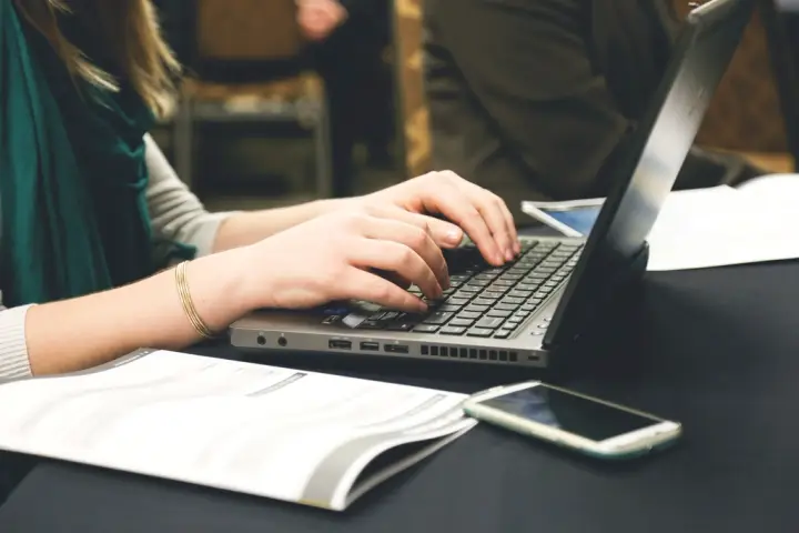 Manos escribiendo en un portátil sobre una mesa de trabajo